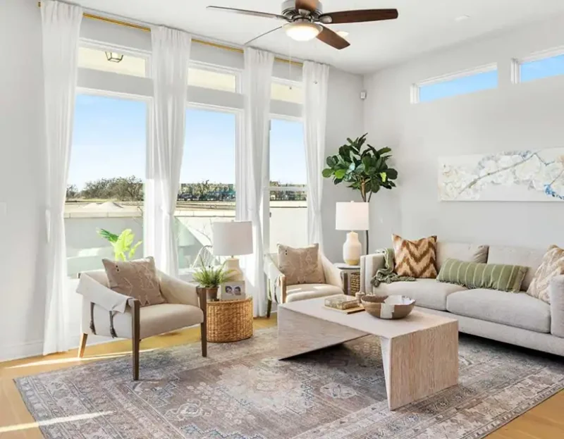 A modern ceiling fan spinning in a bright living room.